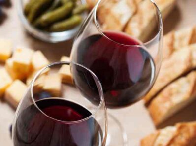 Two glasses of French wine with sliced bread and cheese that is served as french aperitif food in the background that are perfect for a French apéritif